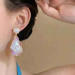 Close-up view of irregular baroque pearl drop earrings with an elegant golden wavy border