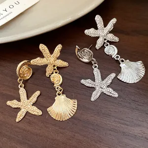 Detail of gold and silver starfish and seashell drop earrings on a wooden background.