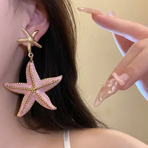 Close-up detail of stylish pink enamel and gold starfish drop earrings worn by a model