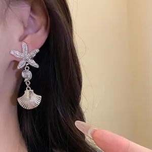 Close-up detail of silver starfish and pleated shell dangle earrings on a model