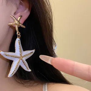 Large white enamel starfish drop earrings with gold-toned beaded edges shown on model.