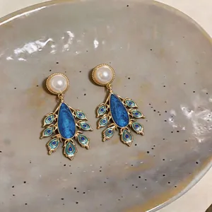 Detailed view of elegant peacock feather drop earrings with blue enamel and pearls