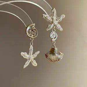 Close-up of asymmetric starfish and pleated seashell drop earrings in silver finish
