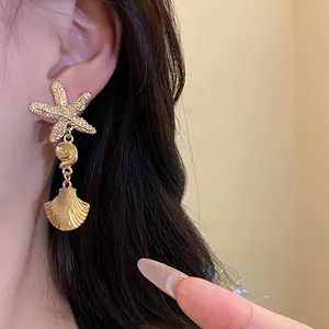 Detailed shot of gold sea star and pleated shell pendant earring worn by a model