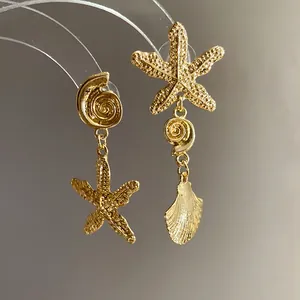 Detailed macro view of golden asymmetric earrings featuring starfish and pleated seashell charms