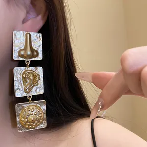 Close-up of retro oversized square drop earrings featuring unique anatomical relief on a model