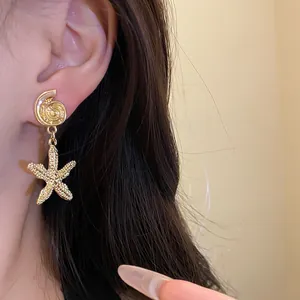 Close-up detailed view of elegant gold starfish and shell dangle earrings worn by a model