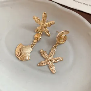Detail view of gold-finished starfish and shell drop earrings on a ceramic tray