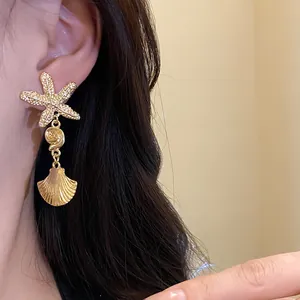 Close-up detail of golden starfish and pleated shell drop earrings on a model's ear