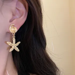 Detailed view of elegant gold starfish and seashell drop earrings worn on a model's ear.