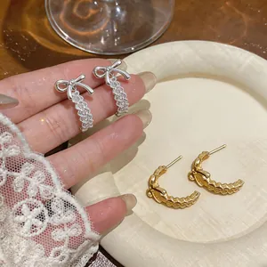 Primer plano de pendientes de tuerca en forma de C huecos con lazo en tonos oro y plata.