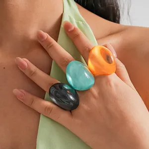 Close-up view of three retro oversized resin rings in vibrant colors worn on a hand