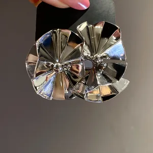 Close-up of silver glossy fan-shaped stud earrings showing high metallic luster and texture