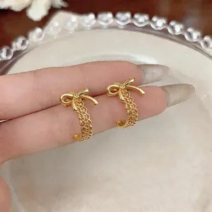 Detalle de elegantes pendientes de lazo dorado en forma de C con diseño calado en dedo