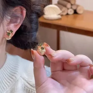 Primo piano di un orecchino a quadrifoglio con zircone verde e dettaglio perla bianca.