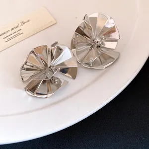 Detailed view of silver metallic ruffled flower stud earrings on white plate