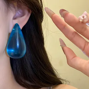 Dettaglio di un grande orecchino a goccia in resina blu indossato con eleganza
