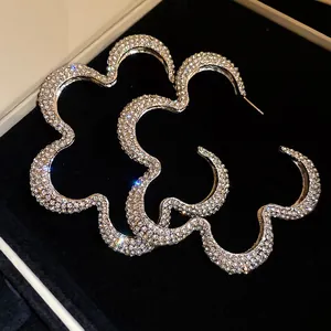 Sparkling rhinestone-encrusted hollow flower hoop earrings on black velvet background.