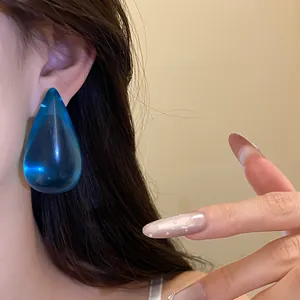 Dettaglio ravvicinato di un orecchino a goccia in resina blu traslucida su una modella.