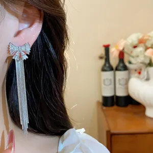 Détail de boucles d'oreilles nœud en argent avec zircons et pompons sur modèle