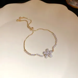 Close-up of elegant gold-toned bracelet featuring a sparkling zircon flower pendant.