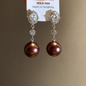 Close-up of elegant silver needle drop earrings with oval rhinestones and brown pearls.
