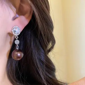 Close-up of elegant silver needle drop earrings with rhinestones and large dark plum pearl