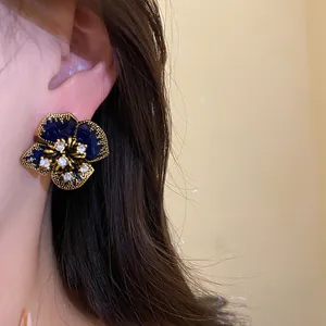 Detailed macro view of vintage floral stud earring with blue enamel and rhinestones on ear
