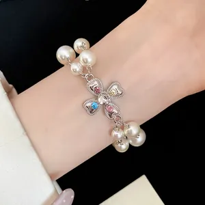 Close-up of a vintage pearl bracelet featuring a colorful rhinestone cross flower charm.
