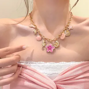 Detail of gold ocean charms necklace with pink flower and shell pendants on model