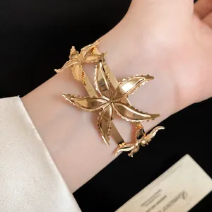 Vista detallada de un brazalete abierto de metal dorado con diseño de estrella de mar