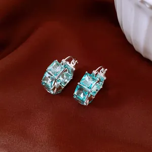 Detailed view of square light blue cubic zirconia hoop earrings on red silk fabric.
