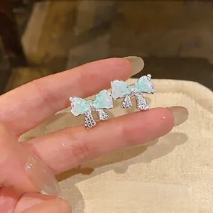 Elegante Schleifen-Ohrstecker mit mintgrünen Harzflügeln und funkelnden Kristalldetails.