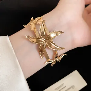Vista detallada de un lujoso brazalete metálico dorado con diseño de estrella de mar.