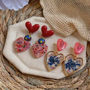 Elegant heart-shaped dangle earrings featuring dried flowers and vibrant glitter details