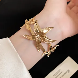 Primer plano de un brazalete dorado con motivos de estrellas de mar en una muñeca.