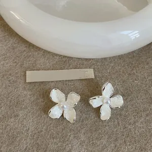 Detailed macro view of French style white enamel flower stud earrings with central pearls.