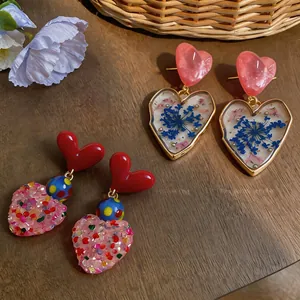 Detailed view of heart drop earrings with dried flowers and glitter accents.