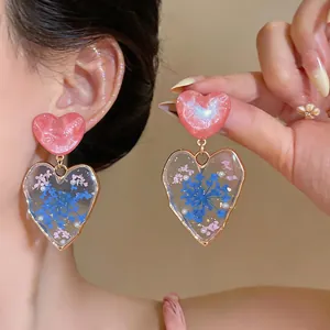 Detail view of heart-shaped earrings featuring pink resin and blue dried flowers.