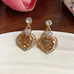 Close-up of elegant gold heart earrings with amber crystal and sparkling rhinestones