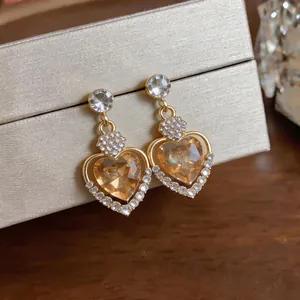 Close-up of golden heart earrings with amber crystals and sparkling rhinestones