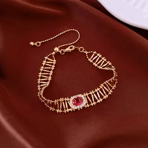 Primo piano di un braccialetto vintage dorato con zircone rosso e design traforato.