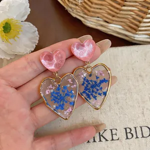 Close-up of heart-shaped earrings with blue pressed flowers and gold-tone borders