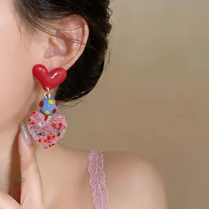 Close-up of vibrant heart-shaped dangle earrings with red and pink textured details