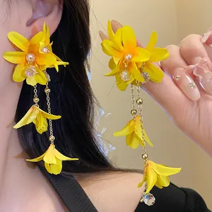Close-up detail view of yellow fabric flower earrings with pearls and long golden tassels