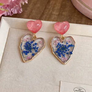 Close-up of heart-shaped drop earrings with real blue dried flowers in clear resin