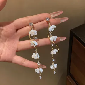 Close-up of elegant long tassel earrings with white resin flowers and sparkling zircons