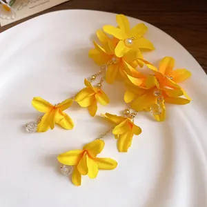 Detailed macro view of yellow fabric flower earrings with pearls and golden tassels