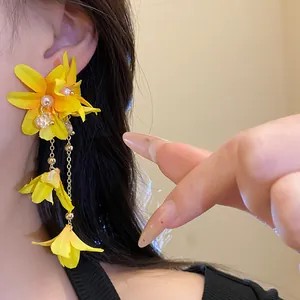 Close-up of yellow fabric flower earrings with pearls and tassels on model's ear