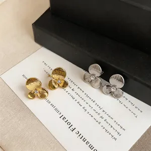 Close-up of gold and silver textured three-petal flower stud earrings with center stones.